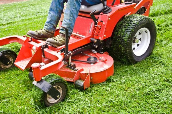 Man on a riding lawn mower that has grass stuck to the wheels. Spring and summer outdoor maintenance.
